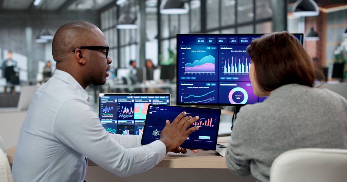 Business Analyst And Marketing Coach Examine KPI Dashboards On Multiple Screens. An African American Woman